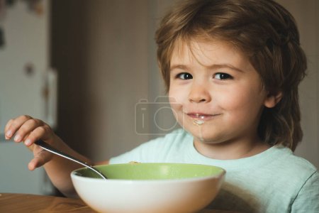 Foto de Pequeño bebé divertido están comiendo. El niño feliz come una cuchara de comida saludable. Comida y bebida para niños. Un chico lindo está comiendo. Retrato de un niño hermoso desayunando en casa - Imagen libre de derechos