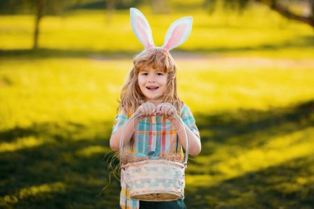 Foto de Feliz Pascua para los niños. Niño con traje de conejo con orejas de conejo cazando huevos de Pascua en el parque - Imagen libre de derechos