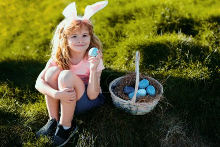 Foto de Feliz Pascua para los niños. Niño en orejas de conejo con huevos de colores jugar y la caza de huevos de Pascua fuera. - Imagen libre de derechos