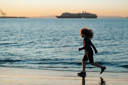 Foto de Un chico corriendo en la playa. Niño feliz correr en el mar en las vacaciones de verano. Vacaciones de verano con niño - Imagen libre de derechos