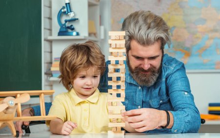 Photo for Father looking at son playing jenga game. Little boy pupil with happy face expression near desk with school supplies. Young happy family father and son schooling math together - Royalty Free Image