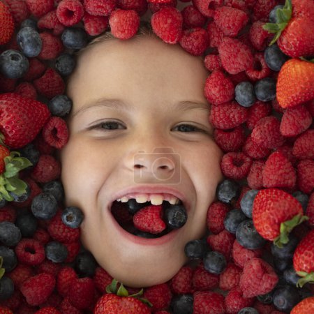 Photo for Fruits for kids. The kids face with fruit and berries. Summer strawberry, blueberry, raspberry, blackberry background. Top view photo of child face in berries background. Healthy kids eating - Royalty Free Image