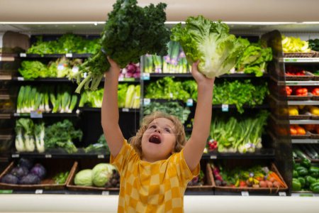 Foto de Niño con lechuga y acelgas. Niño en el supermercado de verduras. Pequeño niño eligiendo comida en la tienda o tienda de comestibles - Imagen libre de derechos