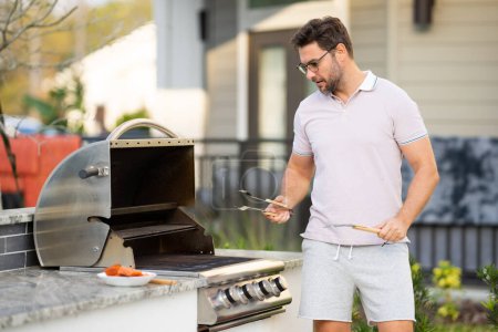Photo for Man cooking meat on barbecue in the backyard of the house. Handsome man preparing barbecue. Barbecue chef master. Cook preparing delicious grilled barbecue food, bbq meat. Grill and barbeque - Royalty Free Image