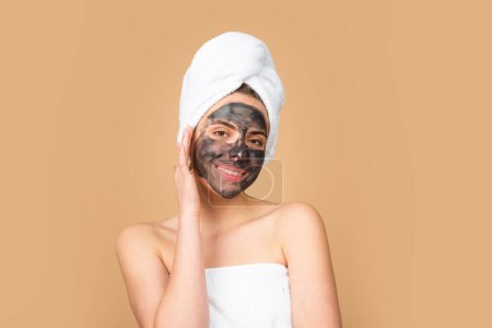 Téléchargez les photos : Masque de boue noire faciale. Belle femme avec masque facial charbon de bois sur le visage. Masques cosmétiques en argile noire. Portrait de belle fille spa. Beauté, santé - en image libre de droit