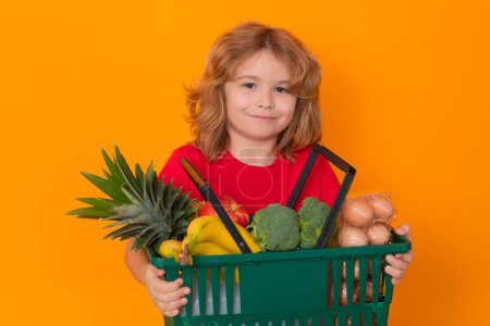 Téléchargez les photos : Portrait d'enfant avec panier d'épicerie, isolé sur fond de studio jaune - en image libre de droit