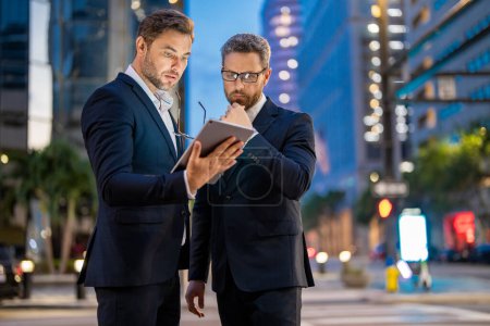 Photo for Business man in night Ney York. Business people discuss a project. The two business teams men team using tablet laptop outdoor. Businessmen looking tablet with business success in night city - Royalty Free Image