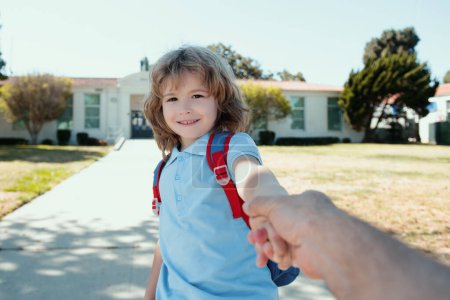 Photo for Little boy holding parent fathers hand with backpack on blurred school building background - Royalty Free Image