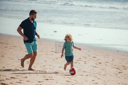 Téléchargez les photos : Père et fils jouent au football ou au football sur la plage pendant les vacances d'été en famille. Papa et enfant jouissant de plein air - en image libre de droit