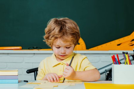 Photo for Back to school. Happy smiling pupil drawing at the desk. Cute little preschool kid boy with teacher study in a classroom. Elementary school and education - Royalty Free Image