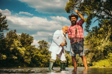 Photo for Fishing team. Retired dad and mature bearded son. Happy fishermen in water. Happy fishermen friendship. Hobby and sport activity. Catch me if you can. Fly fish hobby of men. Successful catch - Royalty Free Image