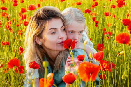 Foto de Hermosa madre e hija en el campo de flores de amapola de primavera. Mamá sostiene a su hija en el prado floreciente. Diseño de primavera - Imagen libre de derechos