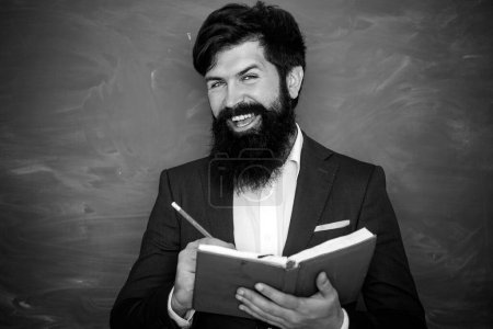 Photo for Bearded professor at school lesson at desks in classroom. Education. Young teacher near chalkboard in school classroom. Friendly teacher in classroom near blackboard desk - Royalty Free Image