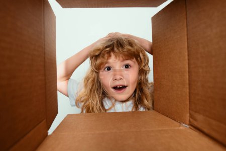 Foto de Gracioso sorprendido niño sorprendido es regalo de apertura y mirando dentro de la caja de cartón. Paquete de apertura para niños - Imagen libre de derechos