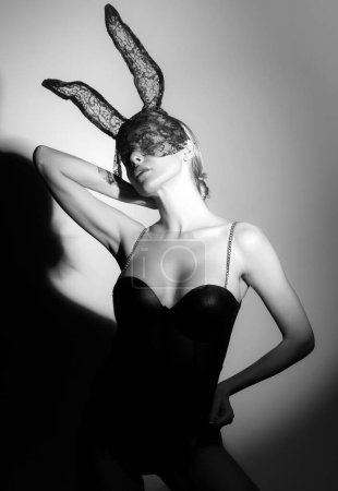 Foto de Hermosa mujer sexy con grandes pechos con máscara de carnaval negro de conejo de Pascua conejo. Chica rubia posando cerca de la pared gris en el estudio. Mujer conejita sexy - Imagen libre de derechos