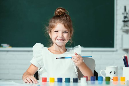 Téléchargez les photos : Enfant fille à l'école dessine avec des peintures. Enfants artiste créativité. Les enfants drôles émotions - en image libre de droit
