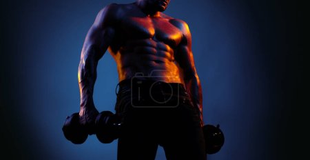 Foto de Modelo Fitness mostrando su cuerpo perfecto. Musculoso chico haciendo ejercicios con mancuerna sobre neón negro fondo azul - Imagen libre de derechos