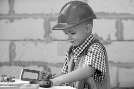 Téléchargez les photos : Portrait de petit constructeur en hardhats avec des instruments de rénovation sur la construction. Garçon constructeur, enfant charpentier avec ensemble d'outils constructeur - en image libre de droit