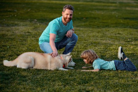 Foto de Sonriente padre y su hijo jugando con perro en el parque con mascota. Niño niño paseo con perrito - Imagen libre de derechos