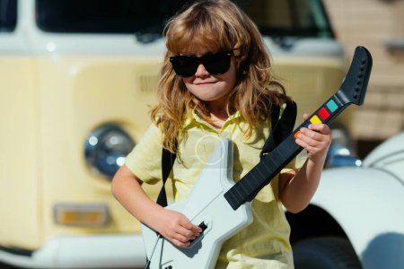 Téléchargez les photos : Mignon enfant garçon chante et joue sur la guitare électrique avec des émotions amusantes. Instruments de musique pour enfants - en image libre de droit