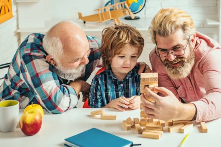 Little boy enjoy time with elderly grandfather and young father. Fathers Day. Happy multi generation family playing Jenga together at home
