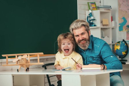 Foto de Pequeño alumno con expresión de cara feliz cerca del escritorio con útiles escolares. Después de la escuela. Tutoría en la escuela primaria - Imagen libre de derechos