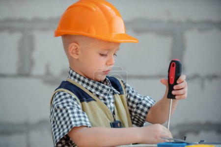 Photo for Child play with supplies, tools saw, hammer, screwdriver, helmet, builder, carpenter. Kids playing in the profession. Little repairman. Kid boy in builders uniform and helmet with repair tools - Royalty Free Image