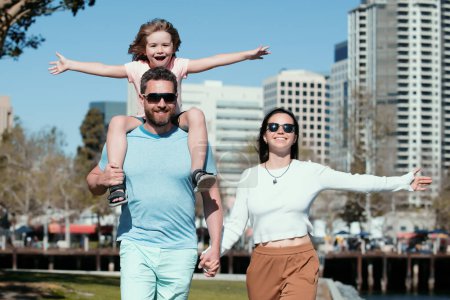 Téléchargez les photos : Portrait de jeunes familles heureuses marchant avec leur enfant sur la ville. Joyeux père qui raccompagne son fils. Personnes concept urbain - en image libre de droit