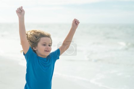 Photo for Excited child funny face. Cute kid run and raised hand on summer sea. Funny expressive emotional boy running on summer beach. Happy boy enjoys run on ocean. Amazed child. Excited child run on beach - Royalty Free Image