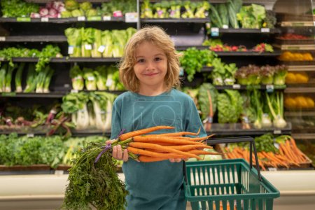 Foto de Niño con zanahoria. Un chico de compras en el supermercado. Tienda de comestibles, la elección de bienes. Compras saludables - Imagen libre de derechos