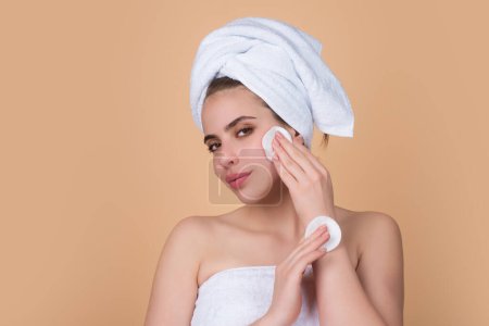 Téléchargez les photos : Removing makeup with cotton pads. Cleaning face with pad. Cosmetic cotton pad. Young woman caring for facial skin using cotton pad in studio. Beauty care and pampering. Daily skincare - en image libre de droit