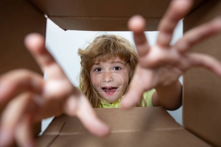 Téléchargez les photos : Enfant de 10 ans ouvre une boîte en carton et en retire un cadeau. Petit garçon regardant dans la boîte de colis et heureux de recevoir une surprise. Enfant prendre à la main cadeau fron boîte ouverte - en image libre de droit