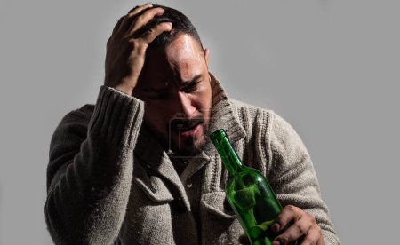 Photo for Alcoholism, alcohol addiction and people concept. Frustrated man with bristle is holding his head, crying and sitting with a bottle in his hands. Depression. Disorders of health - Royalty Free Image