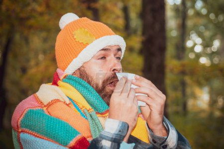 Foto de La persona barbuda estornuda al aire libre. Concepto de enfermedades estacionales. Resfriado común. Alergia, hombre, primavera. Ropa anticuada, estilo retro - Imagen libre de derechos