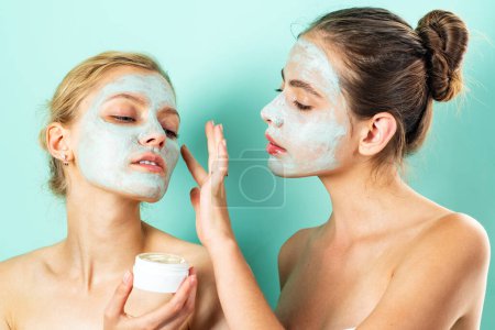 Foto de Dos mujeres jóvenes que aplican crema hidratante en la cara. Foto de amigos cuidadosos que reciben tratamientos de spa. Aseo en casa - Imagen libre de derechos