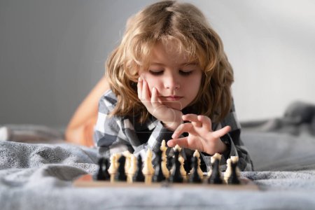 Téléchargez les photos : Un gamin qui joue aux échecs. Enfant pensant à l'échiquier. Apprendre et grandir des enfants, bien-être des enfants. Jeu d'échecs avec des enfants à la maison - en image libre de droit
