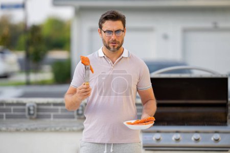 Photo for Grill cook. Chef with BBQ cooking tools. Barbecue and grill. Picnic and barbecue party. Chief cook with utensils for barbecue grill. Barbeque on holiday picnic. Man grilling a salmon fish on BBQ - Royalty Free Image