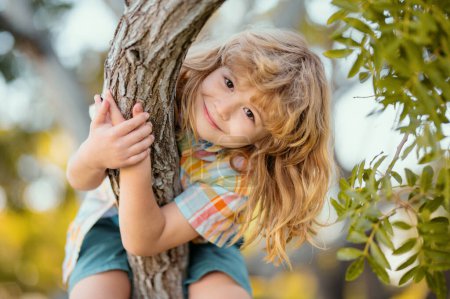 Glückliches Kind, das im Garten spielt und auf den Baum klettert. Junge klettert im Sommerpark auf Baum