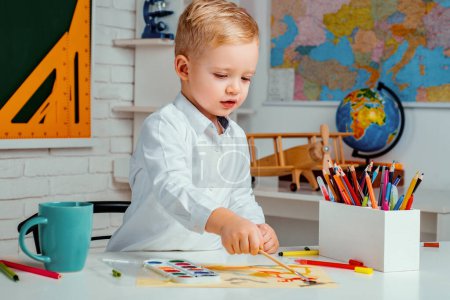 Photo for Cute little preschool kid boy with teacher study in a classroom. Elementary school and education. After school teaching - Royalty Free Image