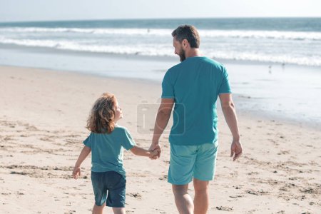 Foto de Padre e hijo caminando sobre el mar. Papá y niño tomados de la mano y caminando juntos. Estilo de vida y vacaciones familiares, concepto de hombres de felicidad - Imagen libre de derechos