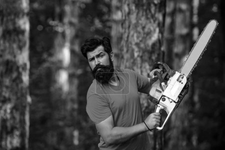 Photo for Professional lumberjack holding chainsaw in the forest. A handsome young man with a beard carries a tree. Harvest of timber. Logging - Royalty Free Image