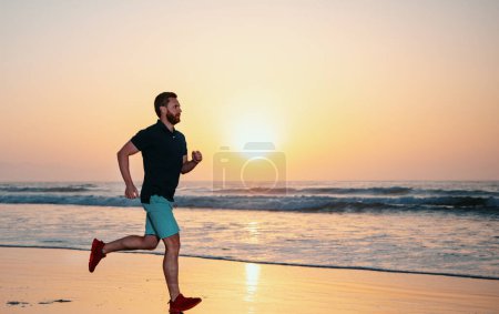 Téléchargez les photos : Toute la longueur de l'homme en bonne santé courir et le sprint à l'extérieur. Coureur masculin. Homme courant sur la plage au coucher du soleil. Concept de mode de vie sain - en image libre de droit