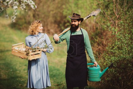 Téléchargez les photos : Concept de Terre. Image de deux fermiers heureux avec des instruments. Un fermier et sa femme debout dans leur champ. Couple d'agriculteurs travaillant dans le champ - en image libre de droit