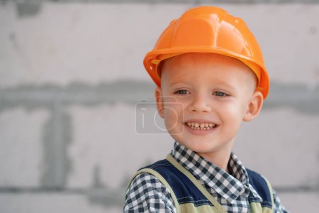 Foto de Un chico con sombrero duro sosteniendo el martillo. Feliz niño sonriente ayudando con herramientas de juguete en el sitio de construciton. Niños con herramientas de construcción. Trabajadores de la construcción - Imagen libre de derechos