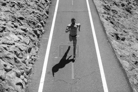 Téléchargez les photos : Toute la longueur de l'homme en bonne santé courir et faire du jogging à l'extérieur. Coureur masculin. Le gars qui fait du sprint sur la route - en image libre de droit