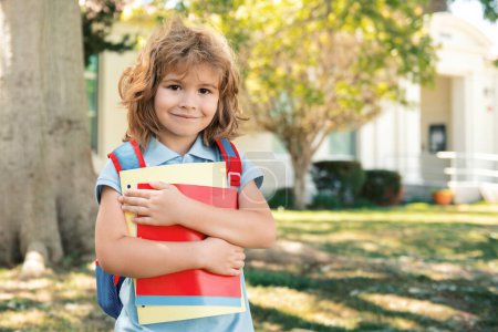 Foto de Alumno de primaria con libro en la mano. Retrato del chico lindo que va a la escuela con su mochila escolar. Inicio de las lecciones - Imagen libre de derechos