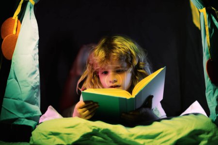 Photo for Kid boy in kids tent reading books. Kids face with night light. Concept of education and reading. Kids development of the imagination - Royalty Free Image