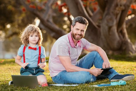 Téléchargez les photos : Entreprise familiale en ligne. Père et fils travaillant sur une télécommande d'ordinateur portable dans le parc - en image libre de droit