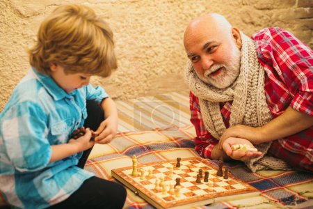 Téléchargez les photos : Enfance. Senior enseignant à son petit-fils à jouer aux échecs. Enfant jouant aux échecs. Concept de grand-père et petit-fils - en image libre de droit