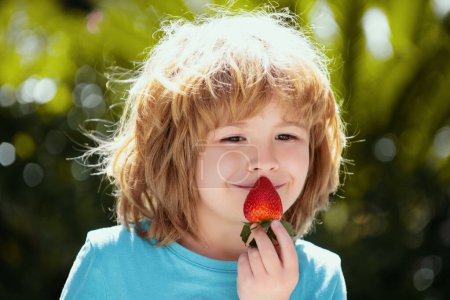 Photo for Healthy kids food. Cute little boy eating a strawberry on green summer background. Close up kids happy face - Royalty Free Image